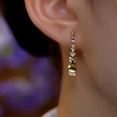 Hammered gold linear drop earring worn on a person's ear