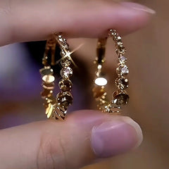 Pair of faceted textured gold hoop earrings held between fingertips