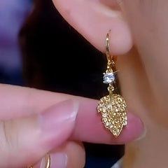 Close-up of gold crystal leaf drop earring held near earlobe