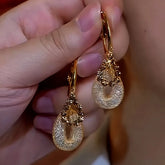 Pair of gold teardrop pave crystal hoop dangle earrings held in hand
