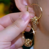 Gold hoop earrings with sparkling crystal ball charm, one held by hand, one worn on ear