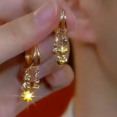 Pair of gold sparkling disc double dangle hoop earrings held in hand