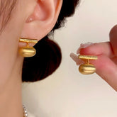 Matte gold engraved bar oval drop earrings: one worn on ear, one held in hand