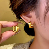 Gold square huggie hoop earrings: one worn on ear, one held in hand