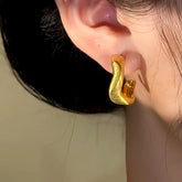 Brushed gold twisted C-hoop earring worn on woman's ear close-up