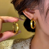 Brushed gold chunky hoop earrings, one held by hand next to a worn earring