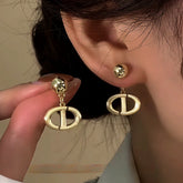 Gold CD logo ball stud dangle earrings, one worn on ear, one held in hand