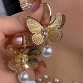 Pair of textured gold butterfly pearl drop earrings held in hand