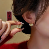 Gold crystal rose earrings: one worn on ear, one held by manicured hand