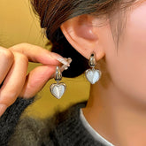 Silver cat's eye heart drop earrings, one worn on ear, one held in hand