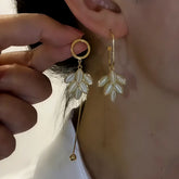Mismatched gold mother of pearl leaf dangle earrings, worn on ear and held