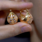 Pair of gold teardrop huggie earrings with opal and CZ accents held in hand