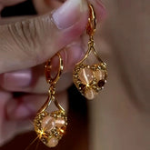 Hand holding gold heart dangle earrings with champagne crystals and cat's eye beads