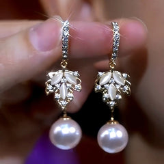 Pair of gold leaf cubic zirconia pearl drop dangle earrings held between fingers