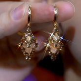 Pair of sparkling champagne gold rhinestone diamond drop hoop earrings held in hand
