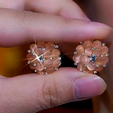 Pair of rose gold pink cat's eye flower CZ stud earrings held by fingers