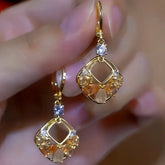 Pair of gold hollow square dangle earrings with orange champagne crystals, held in hand