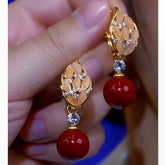 Hand holding pair of women's gold leaf red bead dangle earrings with champagne inlay and crystals