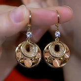 Pair of gold hollow circular drop earrings with opal beads and CZ accents, held in hand