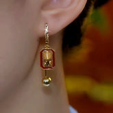 Red enamel gold rectangular bell dangle earring worn on left ear