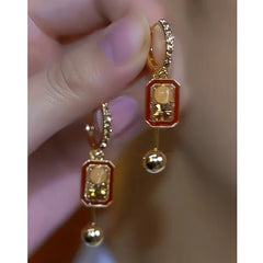 Pair of red enamel gold rectangular bell drop earrings held in hand