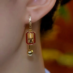Red enamel gold rectangular bell dangle earring worn on left ear