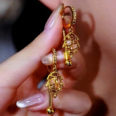 Pair of gold leaf dangle hoop earrings with opal accents held in hand