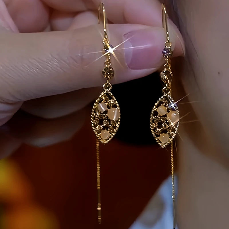Pair of vintage gold filigree teardrop dangle earrings with cat's eye beads, held in hand