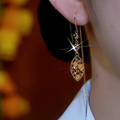 Sparkling gold filigree teardrop dangle earring with cat's eye beads, worn on ear