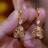 Pair of gold champagne opal ball drop earrings with cubic zirconia, held in hand