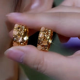 Pair of gold wide hoop earrings with opal stones and champagne crystals held between fingers