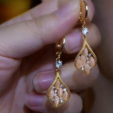 Pair of gold teardrop drop earrings with pink opal & CZ accents held in hand