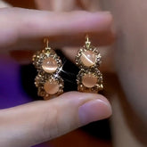 Pair of women's champagne cat's eye gold rhinestone hoop earrings held between fingers