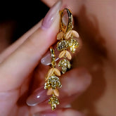 Pair of gold leaf dangle earrings with peach cat's eye stones held by hand