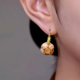 Gold peach cat's eye stone ball dangle earring worn on a woman's ear