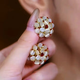 Pair of floral white cat's eye gold stud earrings with red accents held in hand