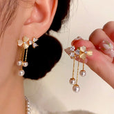 Pair of dainty gold floral pearl drop earrings with crystal bow, one worn one held