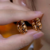 Pair of ornate gold opal crystal hoop earrings held by fingers, closeup