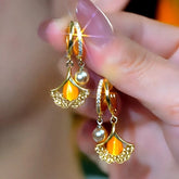 Pair of gold ginkgo leaf amber pearl huggie hoop dangle earrings held in hand