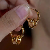 Pair of gem-embellished gold huggie hoop dangle earrings held between fingers