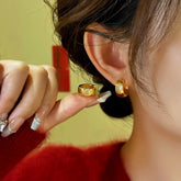 Women's chunky gold huggie hoop earrings with white heart inlay, one worn on ear, one held in hand