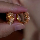 Pair of textured gold cat's eye stone huggie hoop earrings held in hand