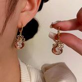 Gold pink money bag dangle earrings with crystal dollar sign, one worn one held