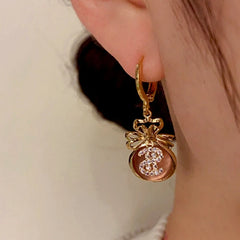 Model showcasing the dangle and style of the 14K Gold-Plated Cat's Eye Stone Lucky $ Bag Earrings