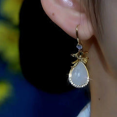 Model showcasing the dangle and style of the 14K Gold-Plated Cat's Eye Stone Purse Ear Hook Earrings