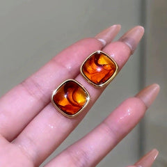 Close-up of amber swirl square gold stud earrings resting on fingertips