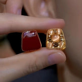 Reversible square huggie earrings, red gemstone and gold cat's eye cat paw sides, held in hand