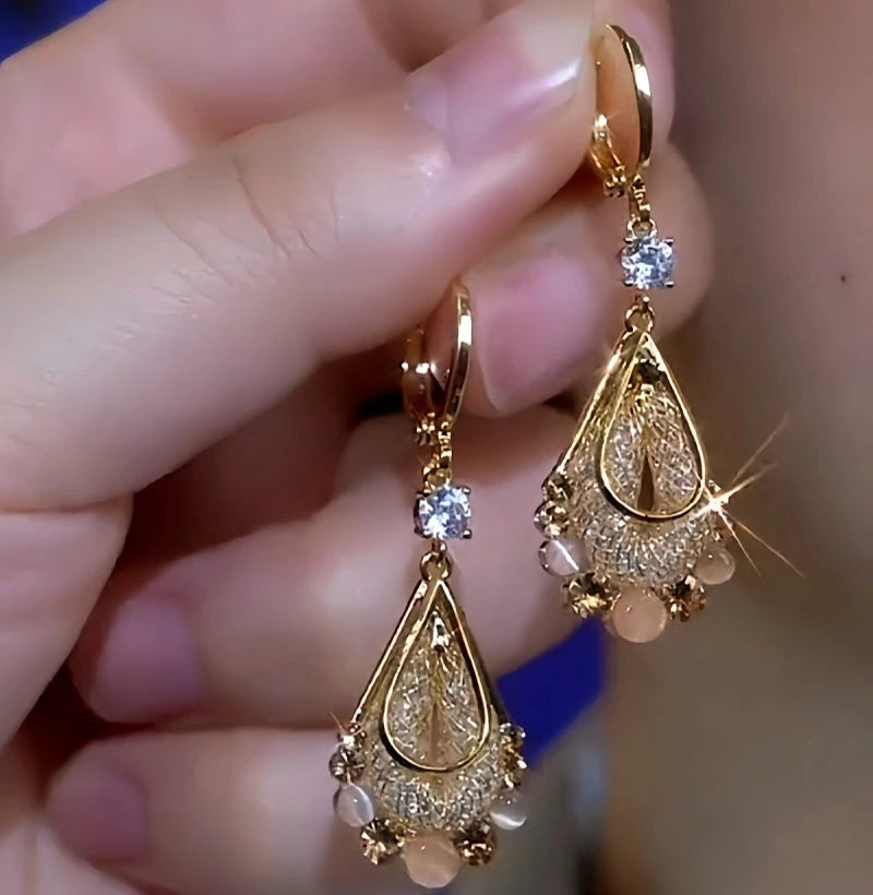 Pair of gold teardrop dangle earrings with crystal and bead accents held in hand