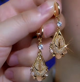 Pair of gold teardrop dangle earrings with crystal and bead accents held in hand