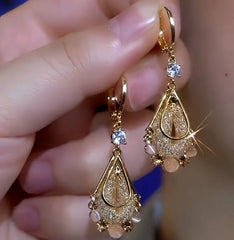 Pair of gold teardrop dangle earrings with crystal and bead accents held in hand